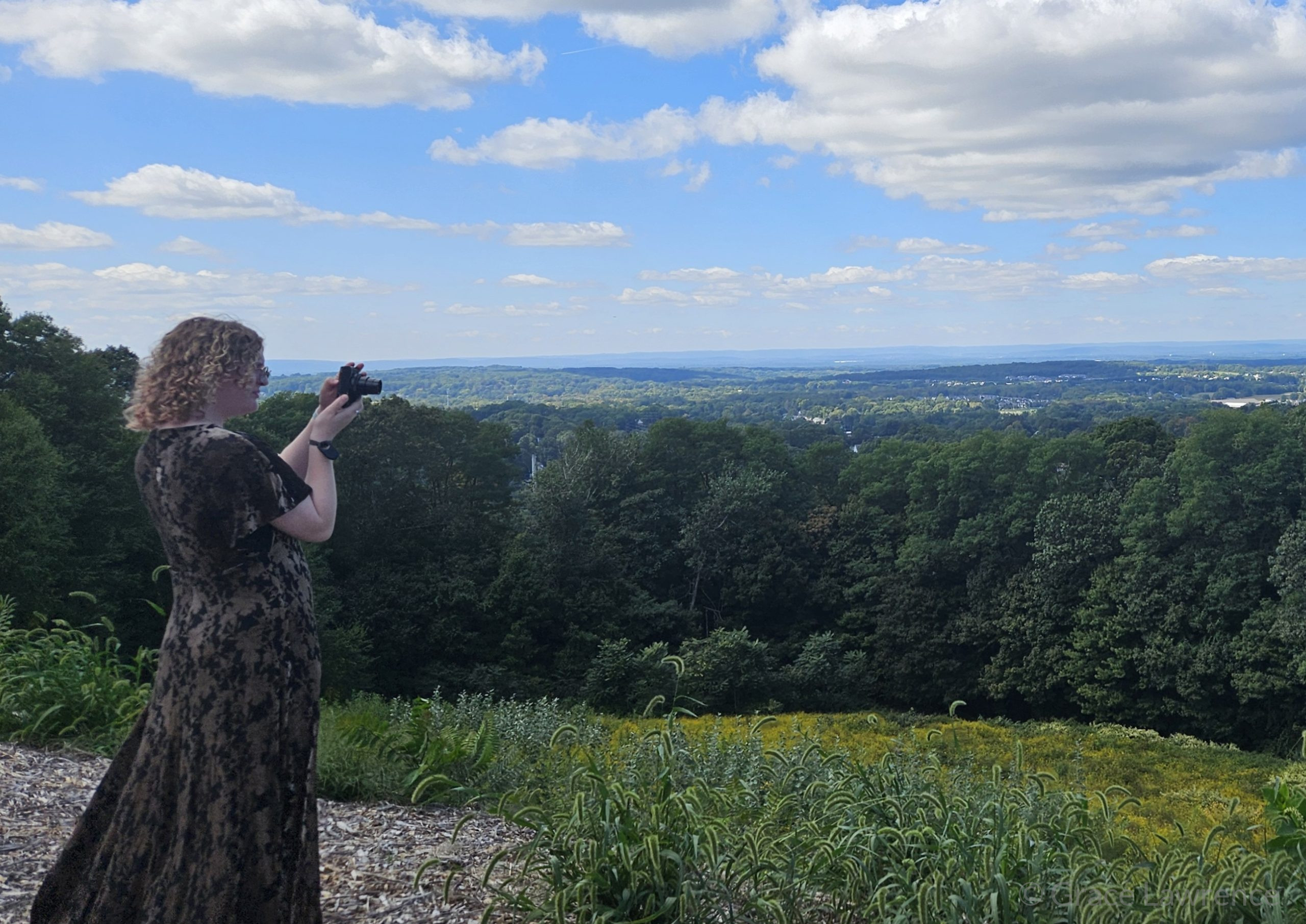 Photograph of myself with curly hair in a dress taking a photograph of a landscape on a clear day