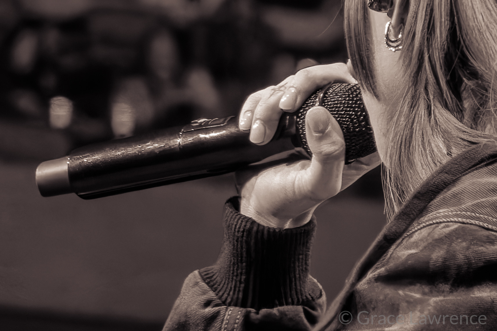 Closeup of Young Miko singing into a microphone. The picture captures the back of her head and her hand holding a microphone.
