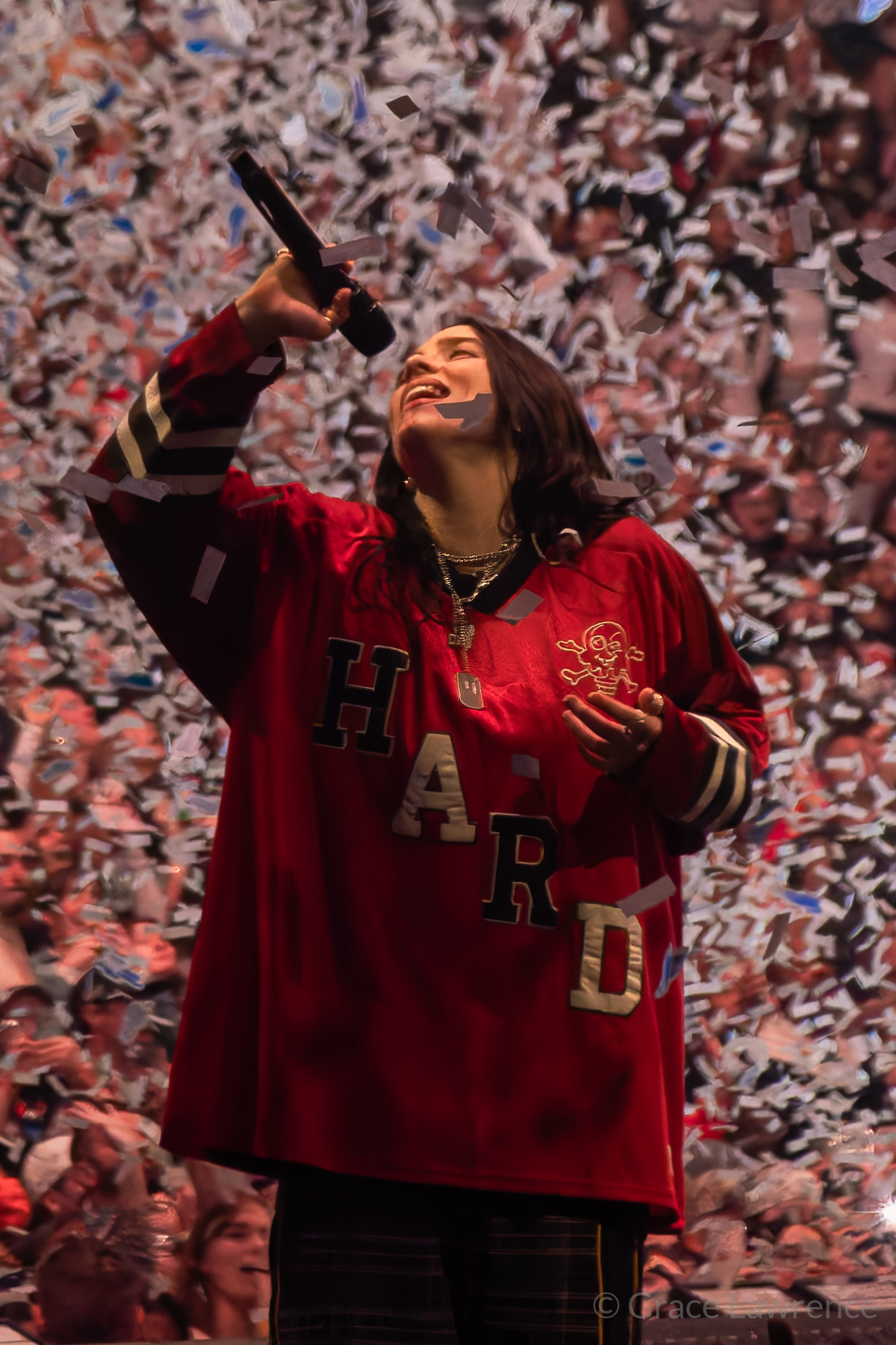 Billie Eilish sings "Birds of a Feather" in a red shirt as she is surrounded by confetti containing her Blohsh shape